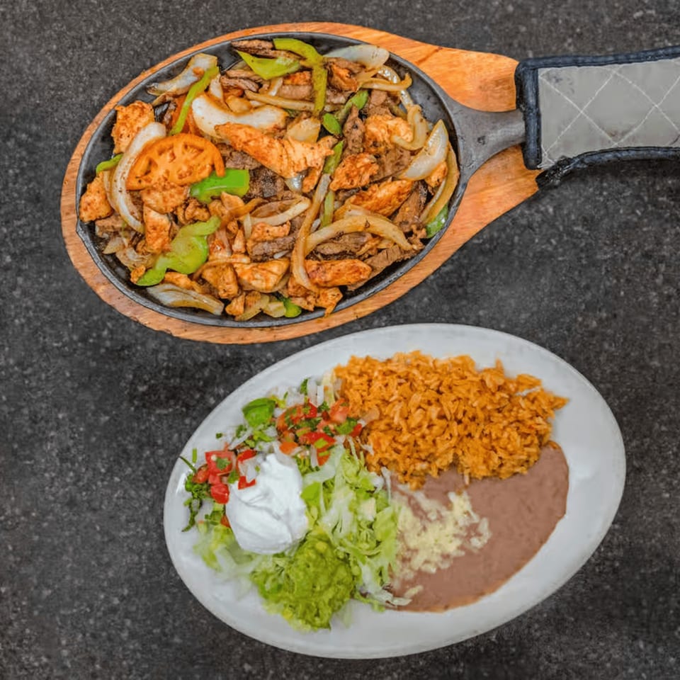 Sizzling chicken and steak fajitas with onions and peppers, served with rice, beans, guacamole, and sour cream.