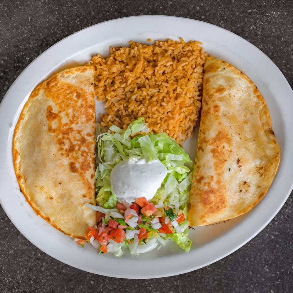 Two golden-brown quesadillas, Mexican rice, and a fresh salad with sour cream and pico de gallo.